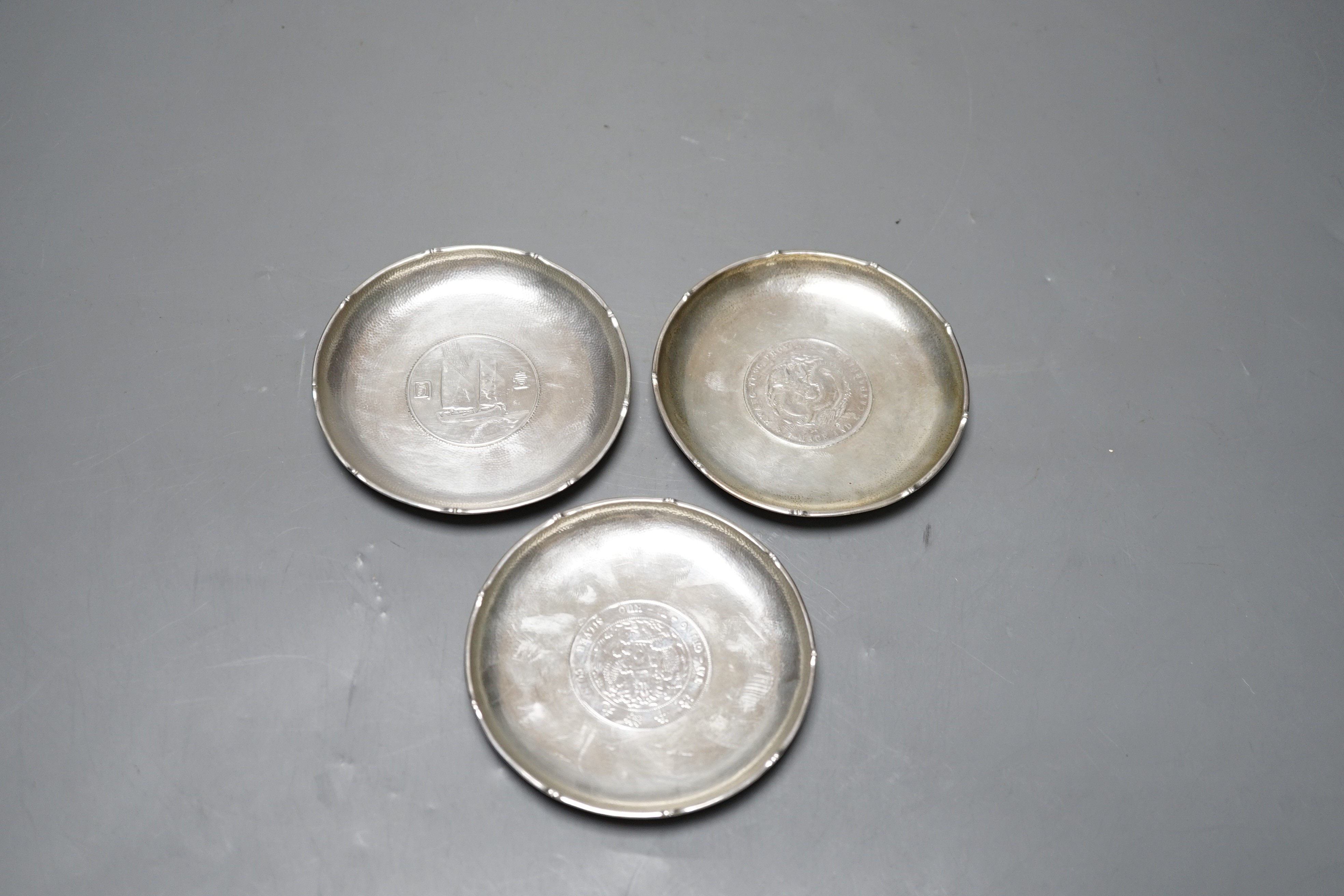 Three Chinese white metal dishes, each inset with coin, maker HC, 94mm, 196 grams gross.